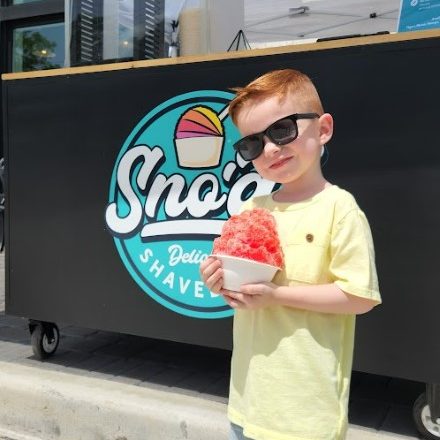 Young kid posing with Sno'd Shaved Ice in front of shaved ice event truck