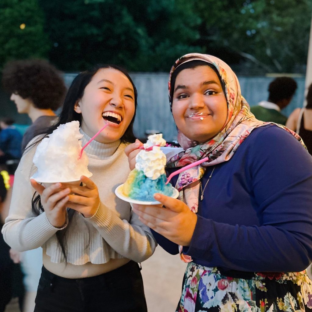 Two girls laughing at outdoor event eating Sno'd Shaved Ice snow cones